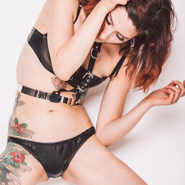 A model wearing a black leather hipster brief with a low-rise design. The brief is handmade from thin, washable glove leather and features soft and supple edges with elastic to hold its shape.