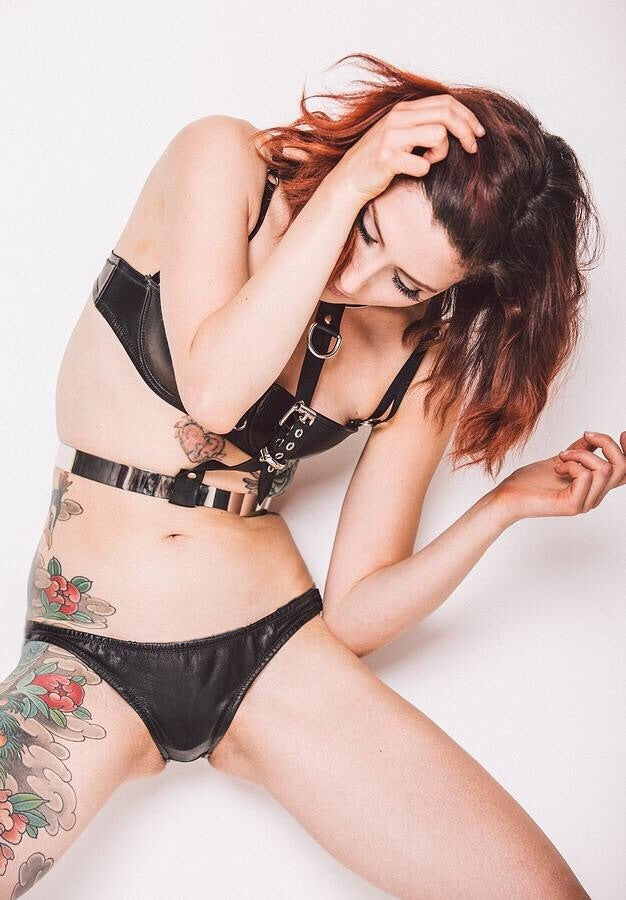 A model wearing a black leather hipster brief with a low-rise design. The brief is handmade from thin, washable glove leather and features soft and supple edges with elastic to hold its shape.